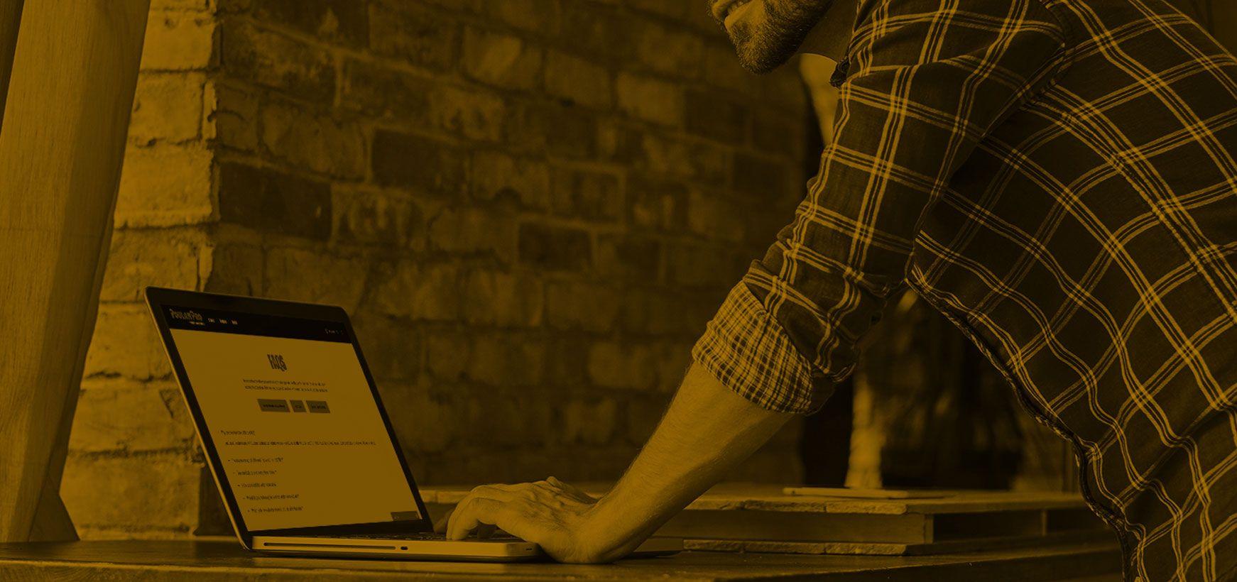 Contact FAQ banner v2 Man typing on his laptop. There is a sepia overlay on the image.